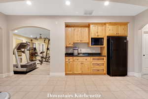 Kitchen with light brown cabinetry, black appliances, arched walkways, recessed lighting, and dark stone countertops