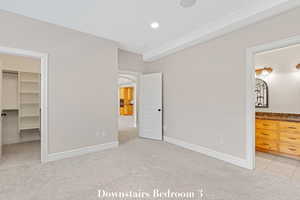 Unfurnished bedroom featuring a walk in closet, light colored carpet, ensuite bathroom, and arched walkways