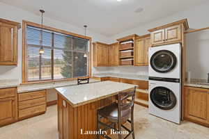 Kitchen featuring estacked washer and dryer, open shelves, a kitchen island, hanging light fixtures, and light stone counters