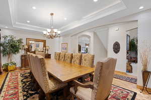 Dining area with arched walkways, a tray ceiling, recessed lighting, ornamental molding, and light wood-type flooring