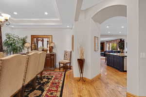 Hall featuring arched walkways, light wood finished floors, healthy amount of natural light, recessed lighting, and crown molding