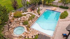 View of pool with a water slide, an in-ground hot tub, a patio area, and a fenced backyard