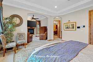 Bedroom with carpet floors, arched walkways, crown molding, a glass covered fireplace, and a tray ceiling