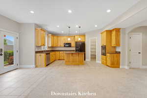 Kitchen featuring recessed lighting, a kitchen island, arched walkways, light tile patterned floors, and dark stone countertops