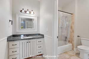Bathroom with vanity, shower / bathtub combination with curtain, and a wainscoted wall