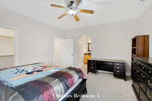 Bedroom featuring arched walkways, light carpet, a ceiling fan, and connected bathroom