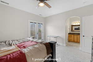 Bedroom with arched walkways, access to outside, light colored carpet, ensuite bath, and a ceiling fan