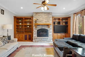 Living area with ornamental molding, ceiling fan, a stone fireplace, and recessed lighting