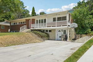 View of front of home featuring stairway, a porch, brick siding, and concrete driveway