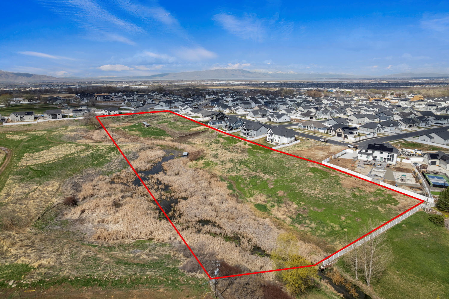 West facing aerial perspective of suburban area with property parcel outlined and a mountainous background
