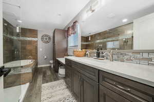 Bathroom featuring tiled tub, vanity, tiled shower, and wood finished floors