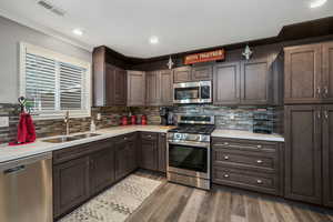 Kitchen with stainless steel appliances, light countertops, dark brown cabinets, wood finished floors, and crown molding