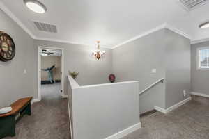 Corridor with an upstairs landing, carpet floors, ornamental molding, and a chandelier
