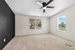 Carpeted empty room with plenty of natural light, a textured ceiling, ceiling fan, and vaulted ceiling