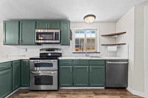 Kitchen featuring green cabinetry, appliances with stainless steel finishes, light countertops, and tasteful backsplash