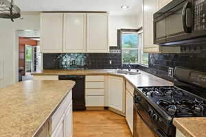 Kitchen with black appliances, light wood-style floors, backsplash, light countertops, and recessed lighting