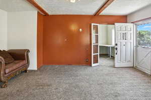 Living area with carpet, a textured ceiling, and beam ceiling