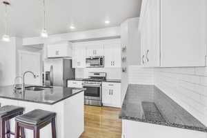 Kitchen with appliances with stainless steel finishes, a breakfast bar area, white cabinetry, pendant lighting, and granite countertops