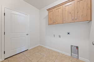 Washroom with hookup for an electric dryer, cabinet space, hookup for a washing machine, and light tile patterned flooring