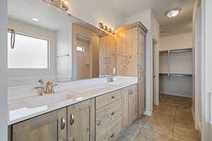 Full bathroom with double vanity, tile patterned floors, and a walk in closet