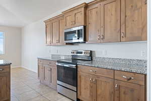Kitchen featuring stainless steel appliances, light tile patterned flooring, light stone countertops, and brown cabinets