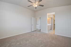 Unfurnished bedroom featuring vaulted ceiling, light carpet, ensuite bathroom, and ceiling fan