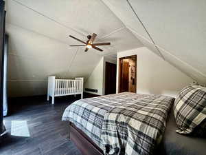 Bedroom featuring dark wood finished floors, lofted ceiling, a textured ceiling, and ceiling fan
