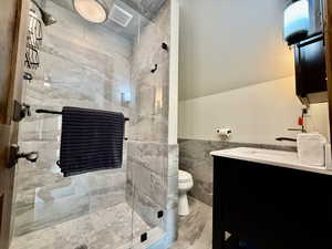 Bathroom featuring tile walls, a stall shower, vanity, marble finish flooring, and wainscoting
