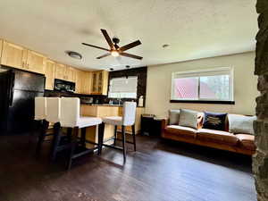 Kitchen with light brown cabinetry, a kitchen bar, black appliances, ceiling fan, and glass insert cabinets
