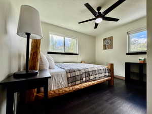 Bedroom with dark wood-style floors, multiple windows, and ceiling fan