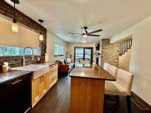 Kitchen featuring open floor plan, a ceiling fan, tasteful backsplash, a breakfast bar area, and dark wood-style flooring