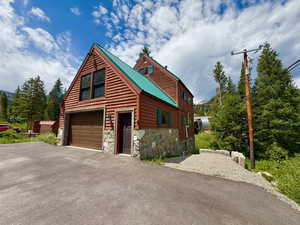 Rustic home with asphalt driveway, stone siding, a garage, and a metal roof