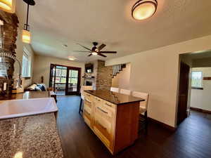Kitchen with a textured ceiling, dark wood-style floors, open floor plan, ceiling fan, and a kitchen breakfast bar