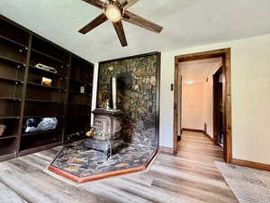 Living room with a textured ceiling, ceiling fan, wood finished floors, and a wood stove