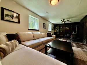 Living area featuring a wood stove, a textured ceiling, wood finished floors, and ceiling fan