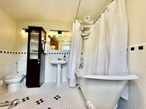 Full bathroom with tile walls, tile patterned flooring, wainscoting, and shower / bathtub combination with curtain