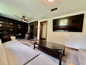 Living room featuring a wood stove, a textured ceiling, and a ceiling fan