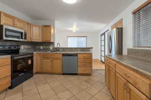 Kitchen with appliances with stainless steel finishes, decorative backsplash, light tile patterned floors, a peninsula, and light brown cabinets