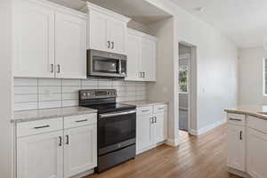 Kitchen featuring appliances with stainless steel finishes, light wood-type flooring, decorative backsplash, white cabinetry, and light stone counters