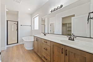 Bathroom featuring a shower stall, double vanity, a soaking tub, and wood finished floors