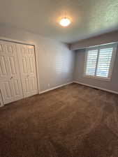 Unfurnished bedroom featuring dark carpet, a textured ceiling, and a closet
