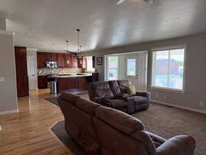 Living room featuring a textured ceiling, light wood finished floors, a ceiling fan, vaulted ceiling, and a chandelier
