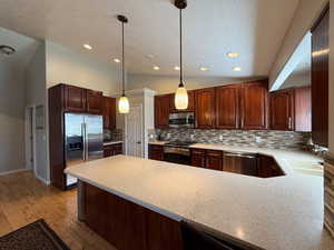 Kitchen with stainless steel appliances, a peninsula, a textured ceiling, light countertops, and tasteful backsplash