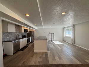 Kitchen featuring dark countertops, a textured ceiling, stainless steel appliances, a center island, and wood finished floors