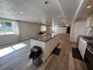 Kitchen featuring open floor plan, light wood-style flooring, a textured ceiling, white cabinetry, and a center island