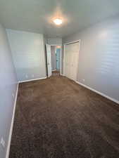 Unfurnished bedroom featuring a textured ceiling, dark carpet, and a closet