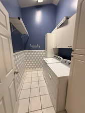 Washroom featuring washer and clothes dryer, cabinet space, light tile patterned flooring, and a wainscoted wall