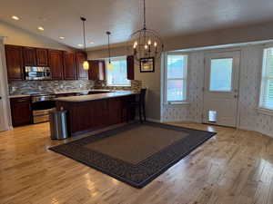 Kitchen with stainless steel appliances, light wood-style floors, a chandelier, tasteful backsplash, and a textured ceiling
