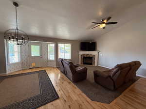 Living room with a chandelier, wood finished floors, a ceiling fan, a stone fireplace, and a textured ceiling