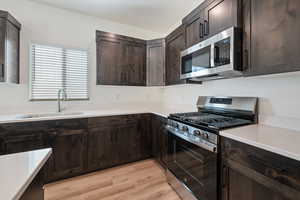 Kitchen featuring appliances with stainless steel finishes, dark brown cabinets, light countertops, and light wood finished floors